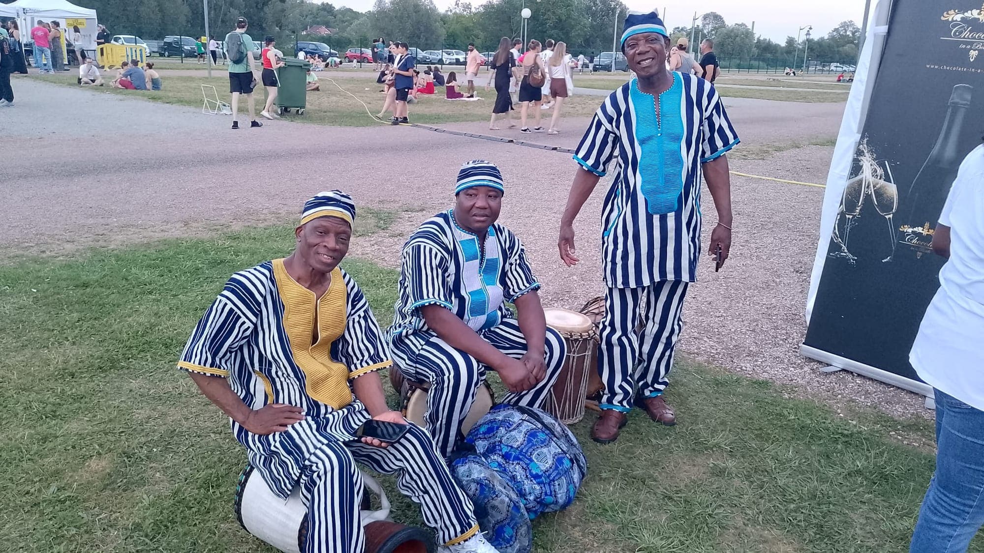 Trois percussionnistes en tenues traditionnelles rayées, installés près de leurs djembés